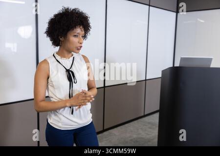 Donna afroamericana che indossa un abbigliamento da lavoro che si presenta in ufficio con un laptop sul leggio Foto Stock