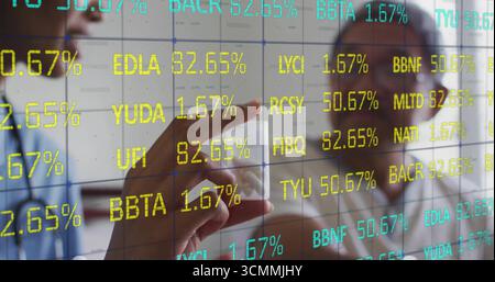 Uomo e donna senior che analizzano i dati finanziari su uno schermo trasparente in ufficio con il dito puntato Foto Stock