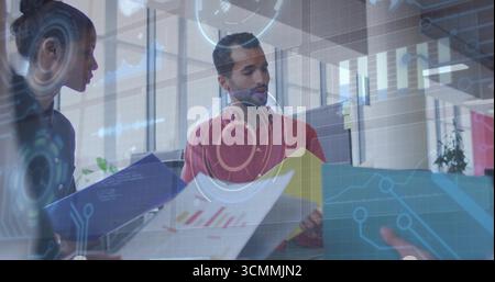 Analisi di un uomo in camicia rossa che interpreta le carte stampate alla scrivania dell'ufficio, con sovrapposizioni di dati Foto Stock