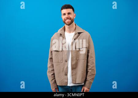 Giovane uomo con barba sorridente in piedi su sfondo blu in un outfit casual Foto Stock