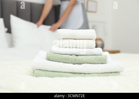 Cameriera che lavora in camera, concentratevi su una pila di asciugamani in spugna sul letto Foto Stock