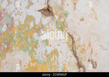 Una profonda crepa attraversa una parete intemprata con strati di vernice verde, gialla e rossa. Foto Stock