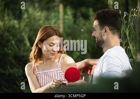 Innesto in posizione di parcheggio. Giovane che si propone alla sua fidanzata mentre si siede su una panchina, la bellezza dice felicemente di sì Foto Stock