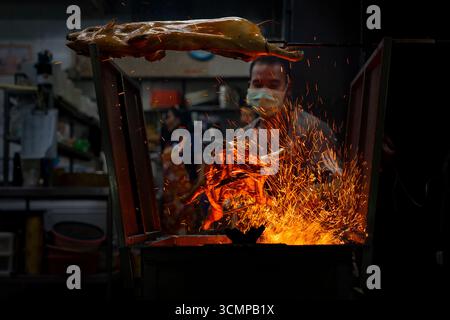 Hatyai, Thailandia - 26 agosto 2024 - l'uomo arrostisce lentamente sulle fiamme aperte in un tradizionale forno a carbone Foto Stock