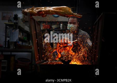 Hatyai, Thailandia - 26 agosto 2024 - l'uomo arrostisce lentamente sulle fiamme aperte in un tradizionale forno a carbone Foto Stock