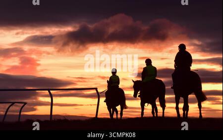 I cavalieri in sagoma si recano al galoppo di Middleham Low Moor nel North Yorkshire mentre l'alba si fa strada su Wensleydale Foto Stock
