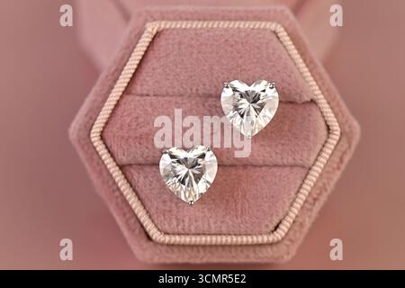 Un paio di orecchini a diamante sono esposti in una scatola di velluto rosa. Gli orecchini sono a forma di cuore e sono realizzati in un materiale chiaro e lucido. La scatola è posizionata Foto Stock
