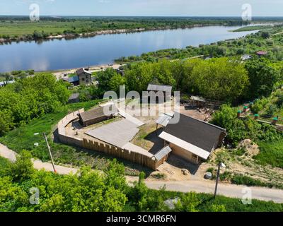 Una prospettiva aerea di un complesso storico con tradizionali edifici in legno e una recinzione in legno, situata su una collina che si affaccia sull'ampio fiume Oka. Foto Stock