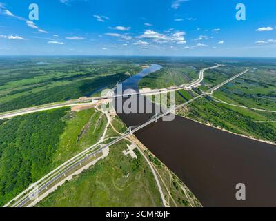 Ampia vista aerea del fiume Oka che si snoda attraverso un lussureggiante paesaggio verde con il ponte Murom e le autostrade circostanti visibili dall'alto. Foto Stock
