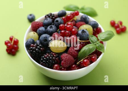 Diversi frutti di bosco e basilico maturi in ciotola su sfondo verde, primo piano Foto Stock