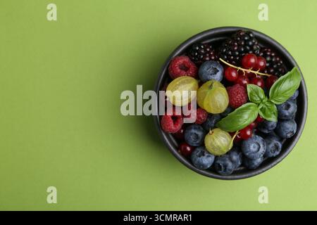 Diversi frutti di bosco e basilico maturi in ciotola su sfondo verde, vista dall'alto. Spazio per il testo Foto Stock