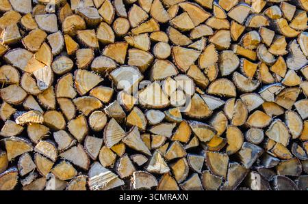 Una vista ravvicinata di legna da ardere impilata in modo ordinato, che mostra la struttura naturale e i motivi del legno. I registri sono tagliati in varie forme e dimensioni Foto Stock