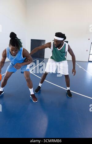 Atleti afro-americani maschili che dribblano e difendono indossando maglie in campo con palla Foto Stock