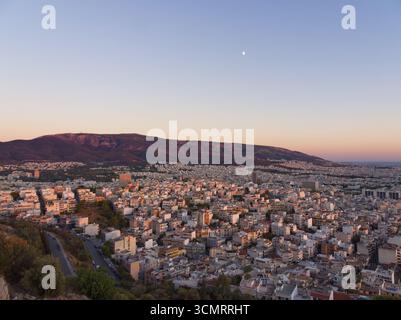 Panorama panoramico della città di Atene all'ora d'oro con la proliferazione urbana, montagne sullo sfondo e luna crescente Foto Stock