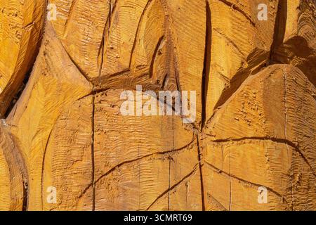 Vista macro dettagliata di una superficie in legno intagliato che mostra segni ruvidi dello scalpello, incrinature e motivi geometrici in calde tonalità arancio-marroni, ideale per il backgro Foto Stock