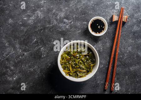 Insalata di alghe sana e fresca con semi di sesamo nel piatto e salsa di soia su sfondo nero, primo piano. Alga il suo elevato contenuto di iodio e calcio ma Foto Stock