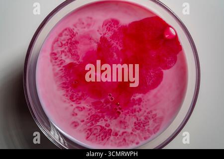 Superficie del latte bianco diluita con succo di lampone rosso fresco in vetro, vista dall'alto. Sfondo astratto di lampone e latte. Colore lampone Foto Stock