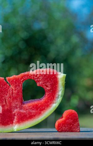 Fetta di anguria rossa fresca e succosa con foro a forma di cuore sullo sfondo della natura nel giardino all'aperto in estate, primo piano. Concetto di felicità, amore, h Foto Stock