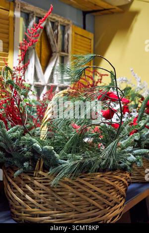 Grande cestino natalizio con rami di pino, cardinali rossi, ornamenti e vegetazione invernale. Una luminosa disposizione floreale natalizia che simboleggia le festività spir Foto Stock