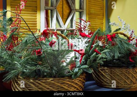 Grande cestino natalizio con rami di pino, cardinali rossi, ornamenti e vegetazione invernale. Una luminosa disposizione floreale natalizia che simboleggia le festività spir Foto Stock