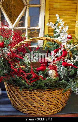 Grande cestino natalizio con rami di pino, cardinali rossi, ornamenti e vegetazione invernale. Una luminosa disposizione floreale natalizia che simboleggia le festività spir Foto Stock