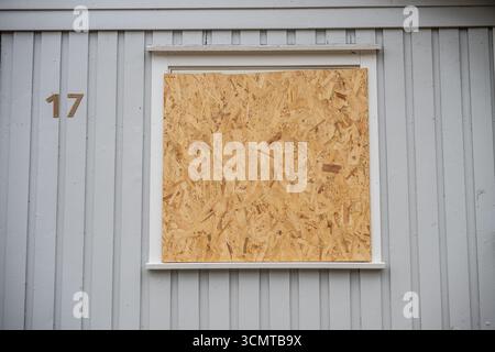 Compensato che copre una finestra di una casa grigia Foto Stock