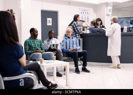Medico donna che ascolta attentamente le preoccupazioni di due diversi pazienti di sesso maschile durante la consultazione sanitaria nell'area di accoglienza ospedaliera. Medico nero che parla e scrive note mediche sugli appunti. Foto Stock