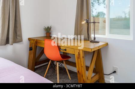 Scrivania in legno in una camera da letto con sedia arancione della metà del secolo e lampada, accanto alla finestra Foto Stock