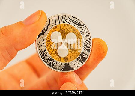 Una mano mostra un gettone fisico Tether, oro e argento, con il logo Bitcoin al centro su uno sfondo semplice, evidenziando il tangib Foto Stock