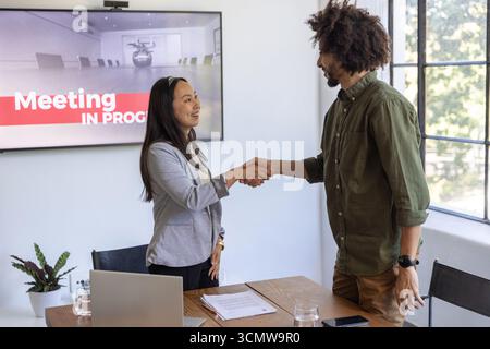 Diversi colleghi in abbigliamento da lavoro che stringono la mano sul tavolo da conferenza, laptop per display Foto Stock