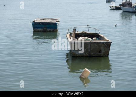 Barcas en el agua y en la orilla en El Rompido con amarres y ancla echados, botes de plastico flotando como boyas, en agua serena de dia soleado Foto Stock