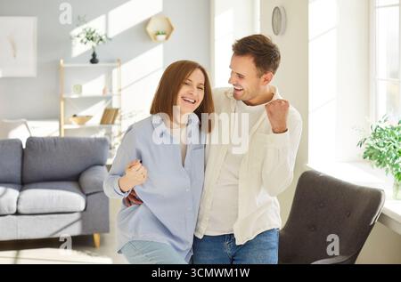 Ritratto di casa, felice felice giovane coppia sposata in posa d'amore, salotto moderno, sì gesto Foto Stock