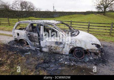 Resti carbonizzati di un veicolo distrutto da un incendio, lasciati abbandonati su una corsia di campagna Foto Stock