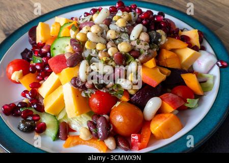 Piatto colorato di insalata con fagioli assortiti, pomodori ciliegini, cetrioli, peperoni, barbabietole, cubetti di formaggio e semi di melograno sul piatto Foto Stock