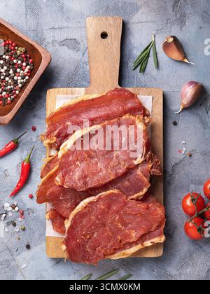 Vista dall'alto di pezzi di maiale affumicato su vassoio di legno circondato da vari ingredienti sul tavolo Foto Stock