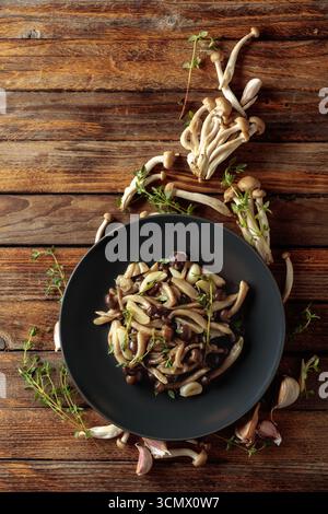 Shimeji fritti con timo e aglio su un tavolo di legno. Funghi freschi e preparati con ingredienti. Cucina tradizionale giapponese. Vista dall'alto Foto Stock