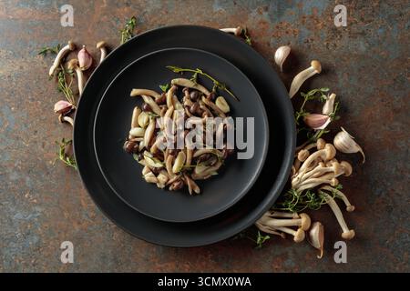 Shimeji fritti con timo e aglio su un piatto nero. Funghi freschi e preparati con ingredienti. Cucina tradizionale giapponese. Vista dall'alto, Foto Stock
