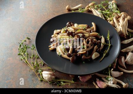 Shimeji fritti con timo e aglio su un piatto nero. Funghi freschi e preparati con ingredienti. Cucina tradizionale giapponese. Foto Stock