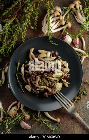 Shimeji fritti con timo e aglio su un piatto nero. Funghi freschi e preparati con ingredienti. Cucina tradizionale giapponese. Vista dall'alto. Foto Stock