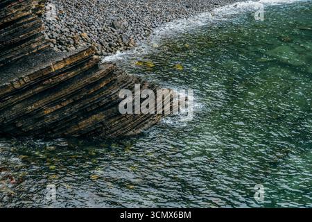 Formazioni rocciose stratificate e Spiaggia di ghiaia sulla costa basca in Spagna. Scogliere sedimentarie stratificate, strati geologici, oceano smeraldo, schemi di erosione Foto Stock