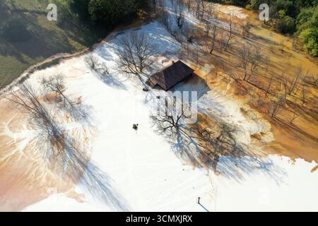 Vista aerea della casa del villaggio che affonda nel mezzo del laghetto di decantazione della miniera di acidi tossici. Geamana, Rosia Montana, Romania Foto Stock