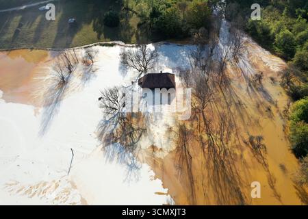 Vista aerea della casa del villaggio che affonda nel mezzo del laghetto di decantazione della miniera di acidi tossici. Geamana, Rosia Montana, Romania Foto Stock