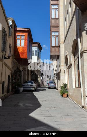 Baku, Azerbaigian - 25 marzo 2025: Una pittoresca strada cittadina con edifici classici, auto parcheggiate e un cielo limpido e soleggiato Foto Stock