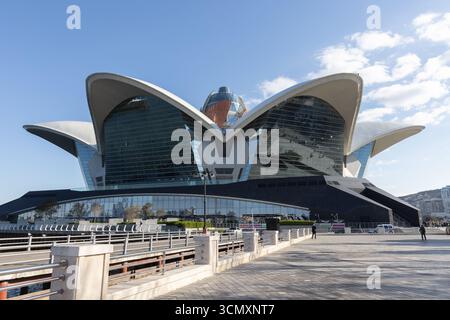 Baku, Azerbaigian - 25 marzo 2025: Esterno del Deniz Mall con ali a forma di stella, la gente cammina per la strada in una giornata di sole Foto Stock