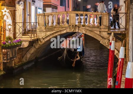 Passerella e gondola nella città di Venezia di notte in Italia. Gondoliere sotto il ponte dei Baretteri sul canale Rio dei Bareteri a San Marco Foto Stock