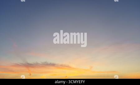 Le nuvole pastello brillano di arancione e rosa sotto un cielo blu che svanisce. Foto Stock