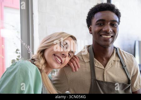 Diversi baristi che si trovano accanto a una finestra con una pianta in vaso in un bar che indossa grembiuli e sorride. Caffè, lavoro di squadra, moderno, ospitalità, amichevole, int Foto Stock