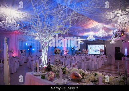 Gli ospiti possono godersi un sontuoso ricevimento di nozze in una sala banchetti splendidamente decorata. I tavoli sono adornati con fiori e splendidi lampadari illuminano Foto Stock