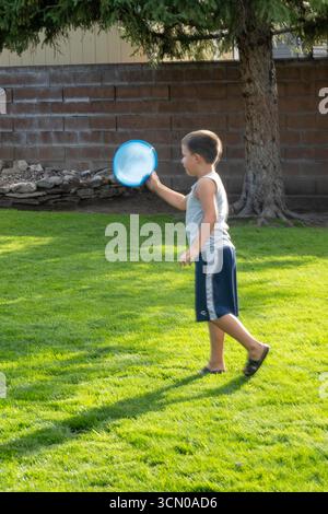 Un bambino di sette anni gioca con un disco volante nel suo cortile in un pomeriggio estivo di sole, 2025, Great Falls, Montana, Stati Uniti Foto Stock