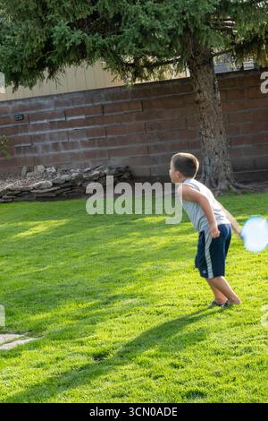 Un bambino di sette anni gioca con un disco volante nel suo cortile in un pomeriggio estivo di sole, 2025, Great Falls, Montana, Stati Uniti Foto Stock